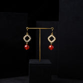 Close-up of elegant red agate and zirconia gold-plated quatrefoil dangle earrings on a black velvet display. Highlights the vibrant red agate beads, sparkling zirconia, and intricate gold setting for Stone World jewelry in Singapore.