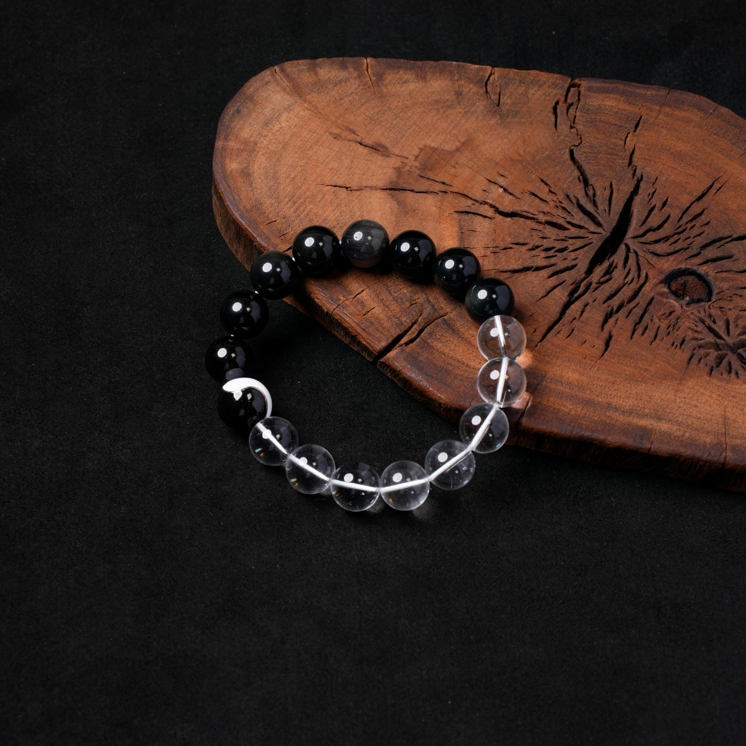 Nuwa Stone's "Clarity & Shadow Balance" stretch bracelet, featuring polished silver obsidian and clear quartz beads, with a central white yin-yang motif on a black bead, elegantly displayed on a dark wooden board.