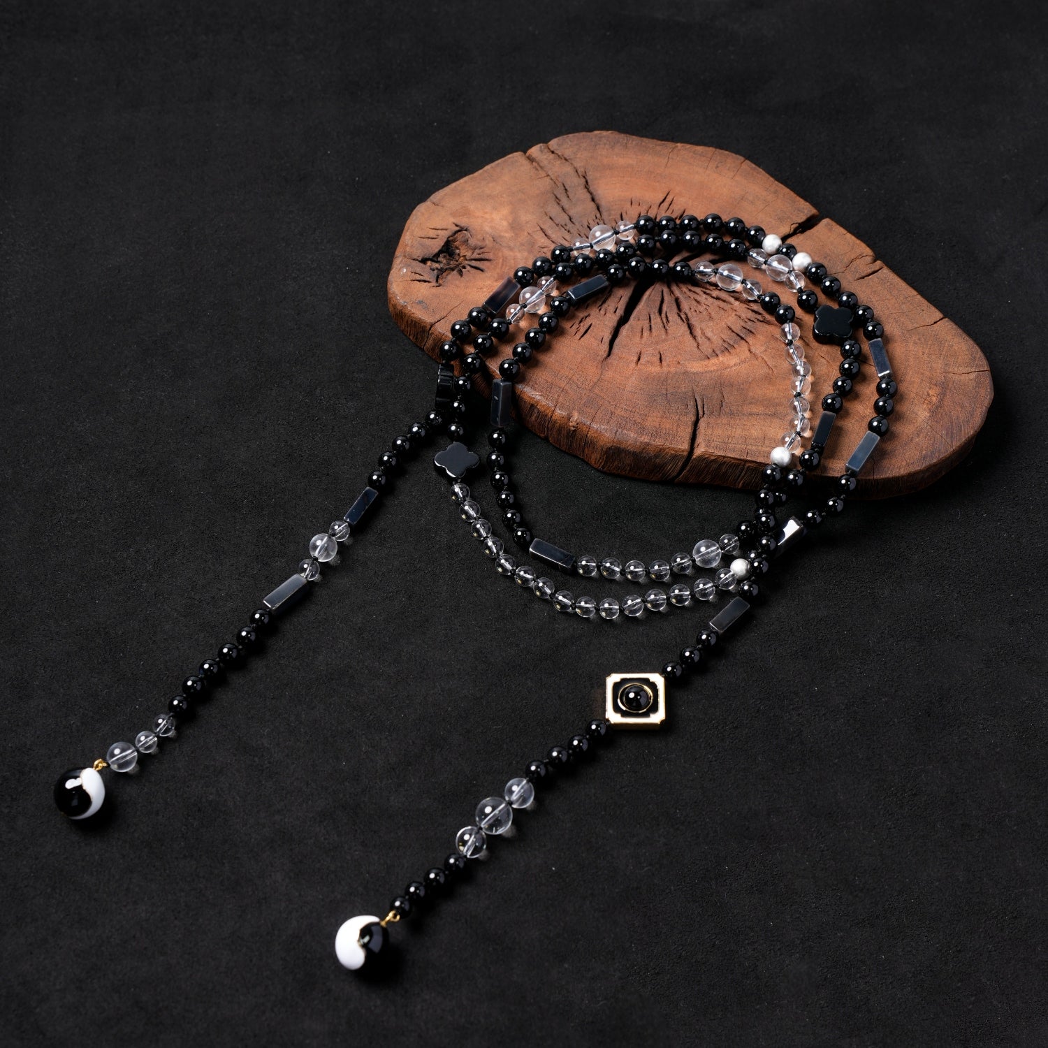 Nuwa Stone's "Four Symbols Begonia" multi-strand convertible necklace, featuring black onyx and clear quartz beads, black begonia-shaped charms, and black and white yin-yang end pieces, elegantly displayed on a dark wooden board.