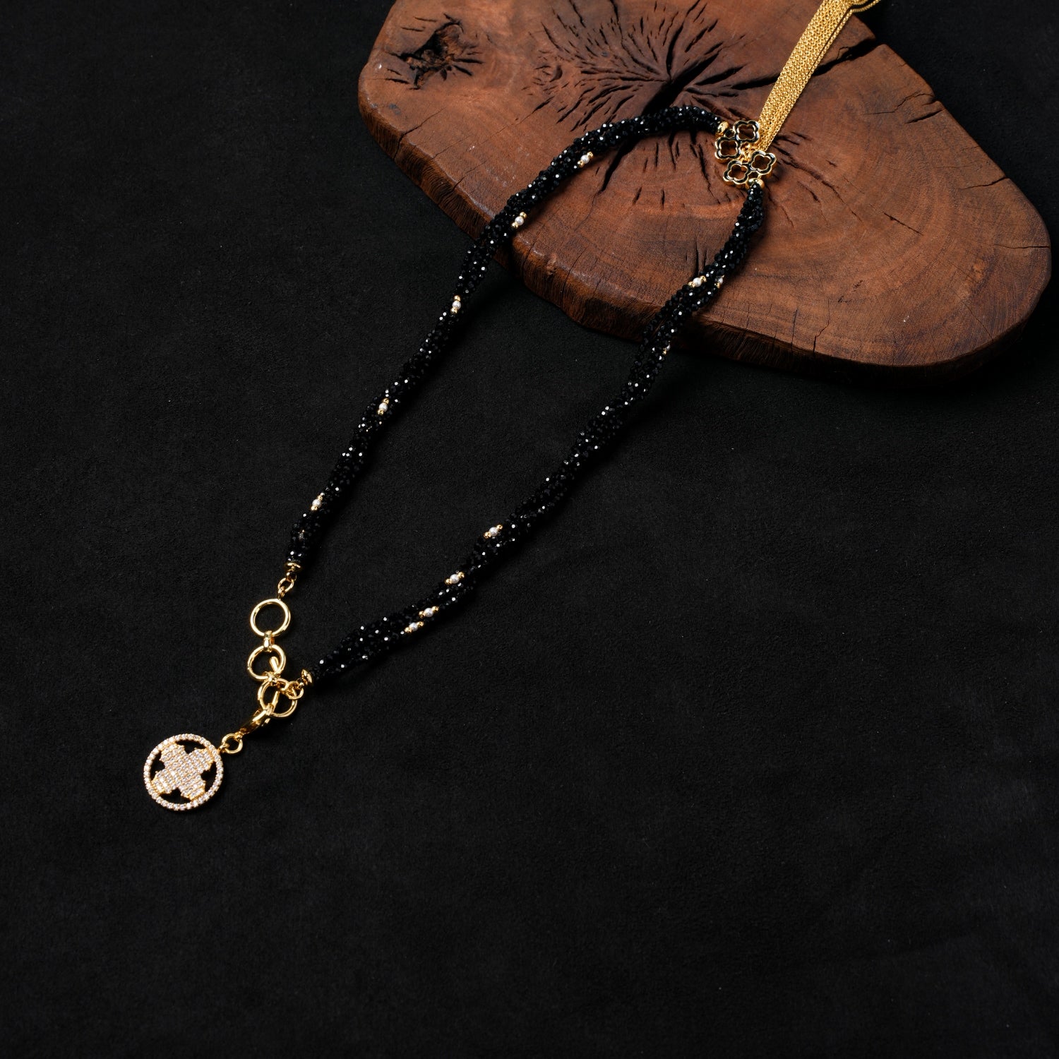 Another full view of Nuwa Stone's "Ink Begonia Cascading Snow" black spinel and pearl necklace, displaying its elegant drape and the gold-plated adjuster chain with a zirconia-paved quatrefoil charm, on a dark wooden board.

