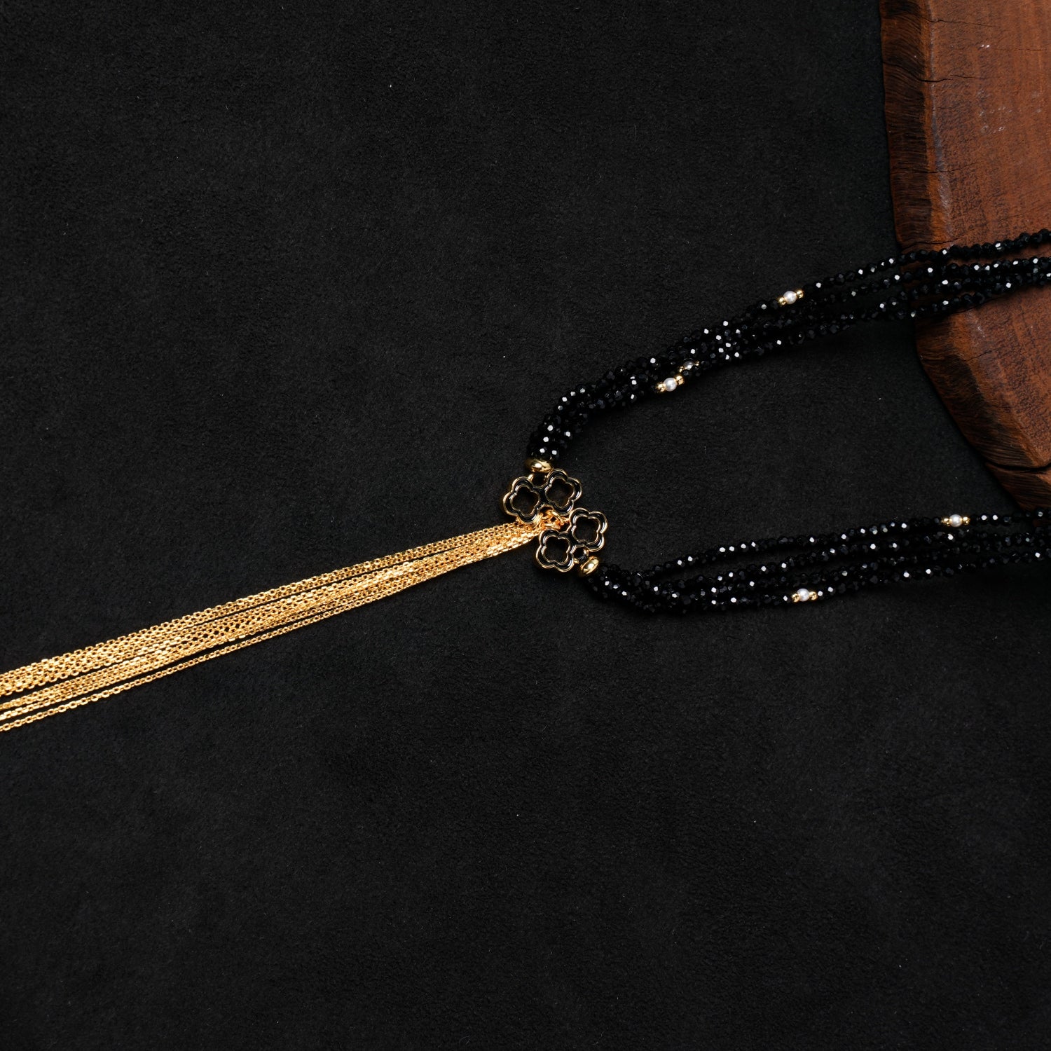 Close-up of the central gold-plated quatrefoil charm and the opulent gold-plated chain tassel from Nuwa Stone's "Ink Begonia Cascading Snow" necklace, showing the intricate design against the sparkling black spinel beads.