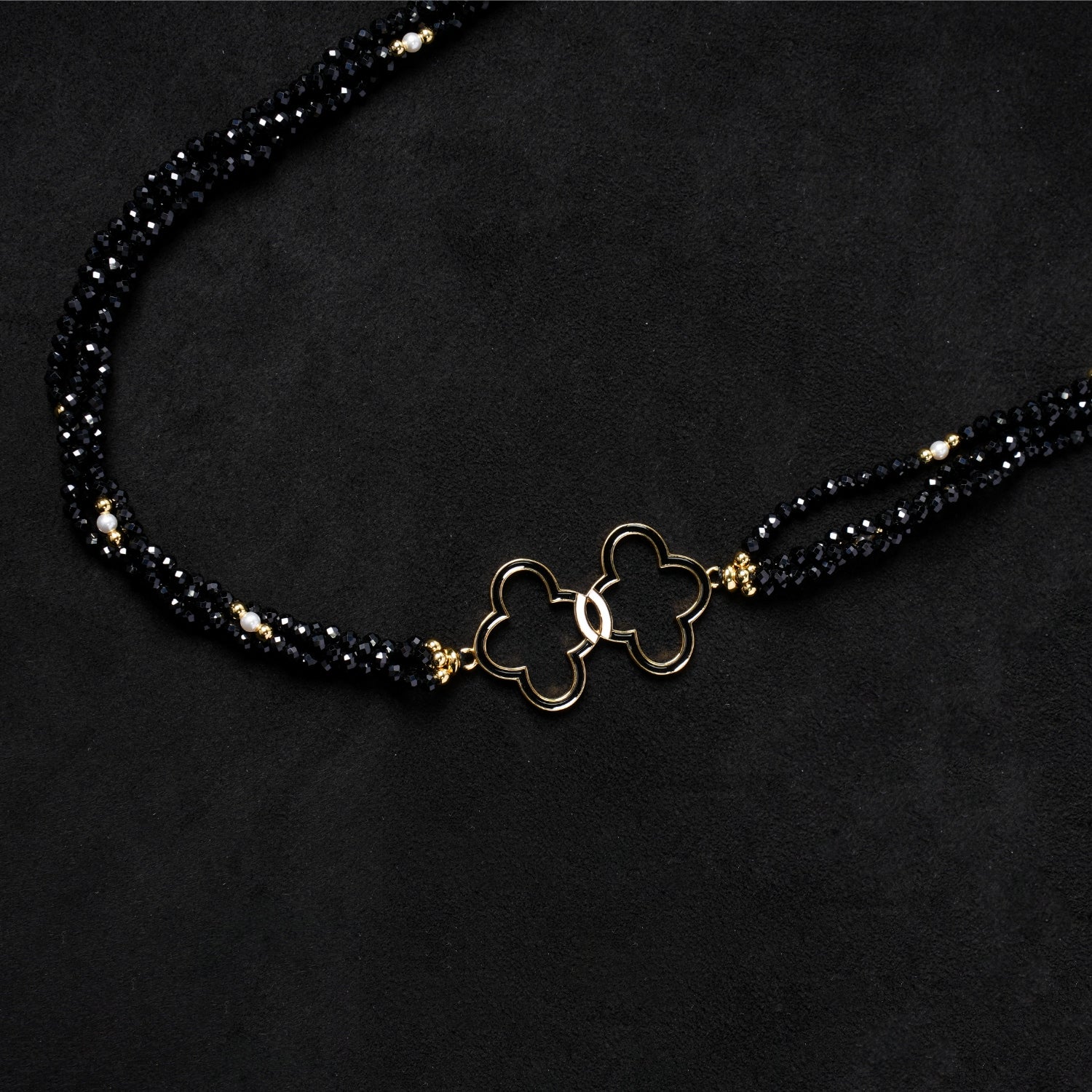 Close-up of the elegant gold-plated double quatrefoil charm at the center of Nuwa Stone's "Nightfall Galaxy Cascade" necklace, flanked by shimmering black spinel beads, showing the intricate details.