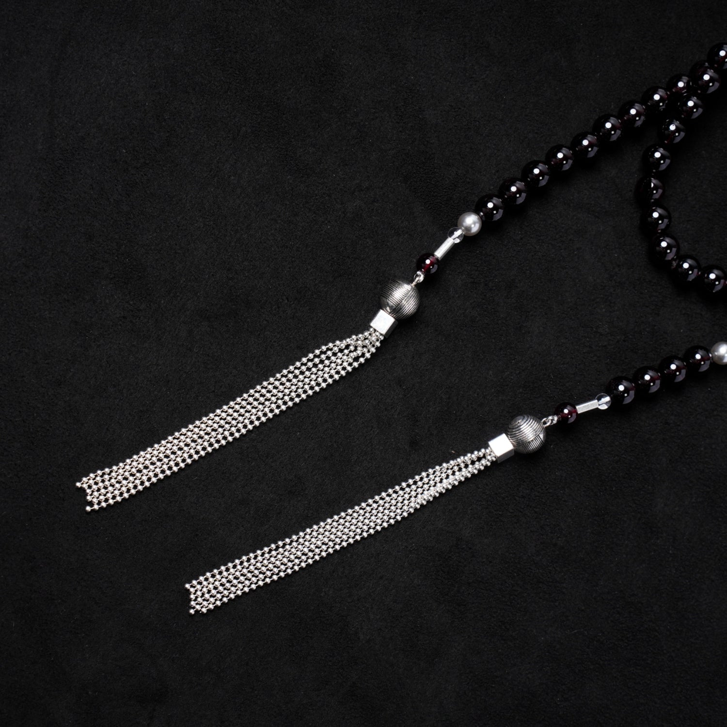 Close-up of the two elegant sterling silver chain tassels, suspended from textured silver caps, which form the distinctive ends of Nuwa Stone's "Twilight Pearl Radiance" garnet necklace.