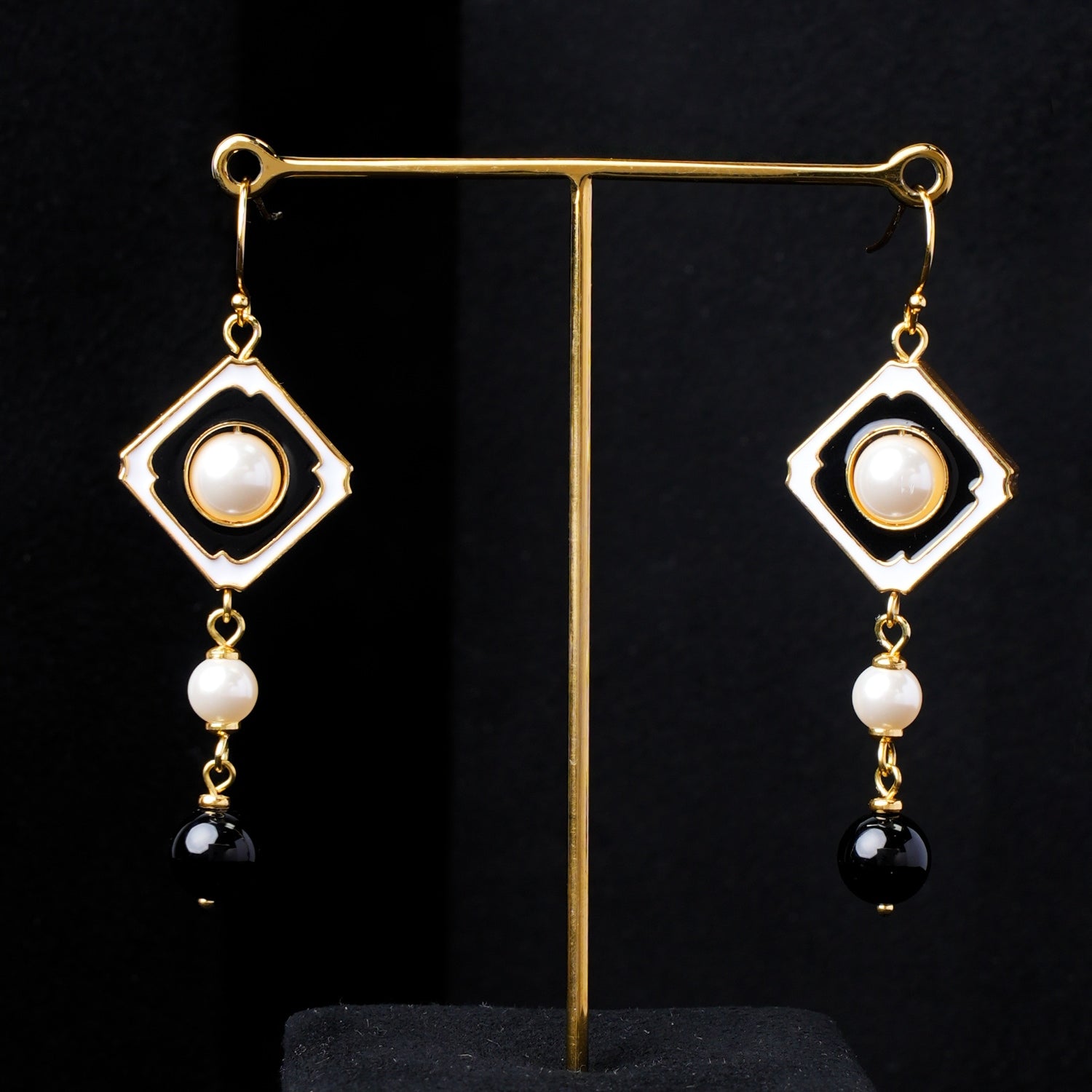 Close-up of the reverse side of Nuwa Stone's Yin Yang Harmony gold-plated dangle earrings. Focuses on the detailing of the square frame, pearls, and black onyx beads from the back perspective.
